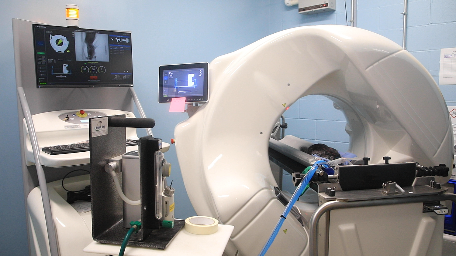 CT scanner in operation with patient inside and monitors displaying scans